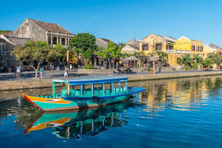 multicoloured fishing boat and yellow pastel coloured buildings reflecting in the Thu Bon River at Hoi Ann Old Town riverfront, Vietnam
