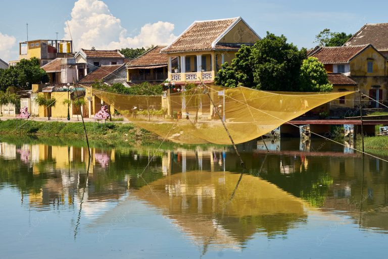 Fishing net above the Thu Bon River and yellow pastel coloured houses at Hoi Ann Old Town riverfront, Vietnam