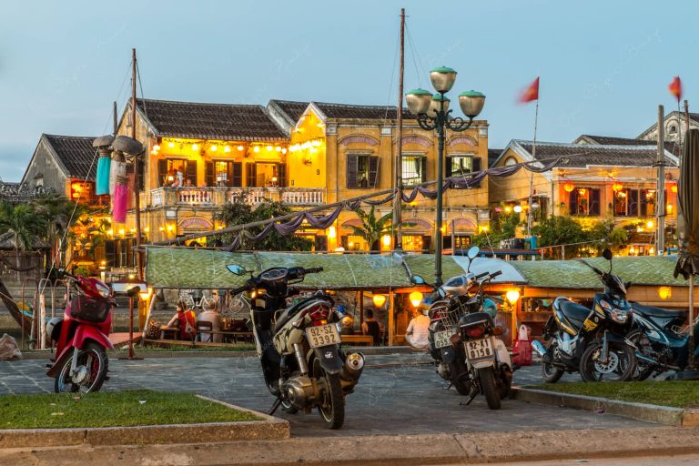 Moored fishing boat restaurant at Thu Bon River and illuminated restaurant buildings at Hoi Ann Old Town riverfront, Vietnam