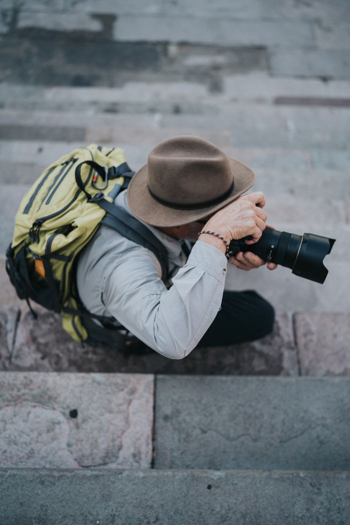 Man with backpack and camera crouching on steps outdoors.