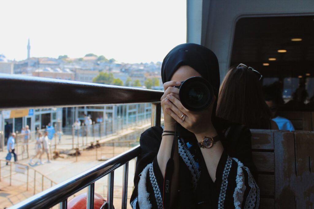 Woman in headscarf photographing cityscape from train with Canon EOS camera