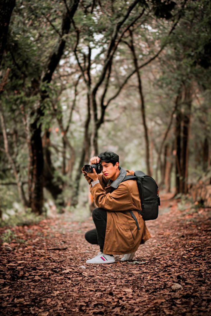 A young adult male photographer captures nature in an autumn forest setting.