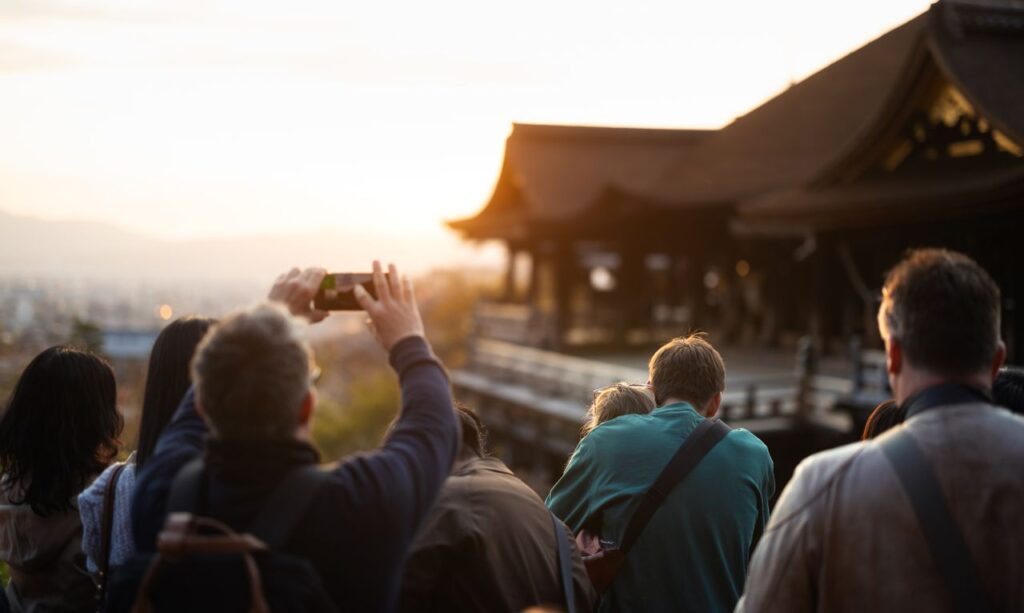Tourists photographing a beautiful temple in Kyoto during a vibrant sunset.