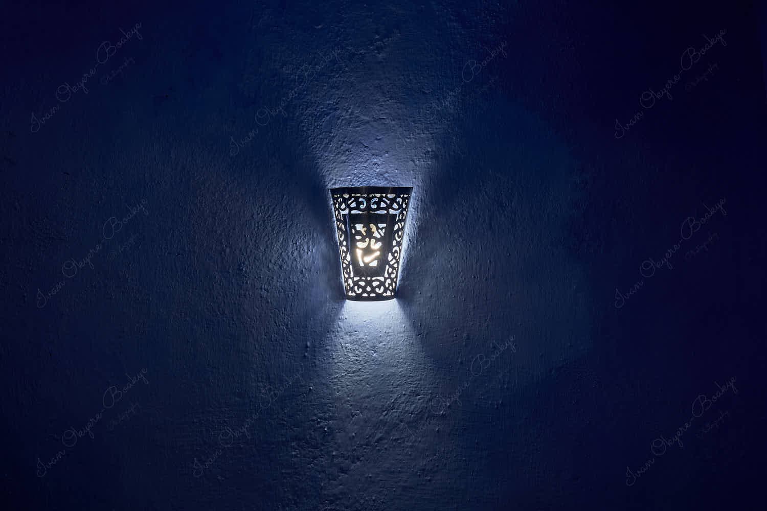 Traditional arabic style wall mounted lamp with light rays creating an abstract pattern on a dark blue textured wall background, Chefchaouen, Morocco