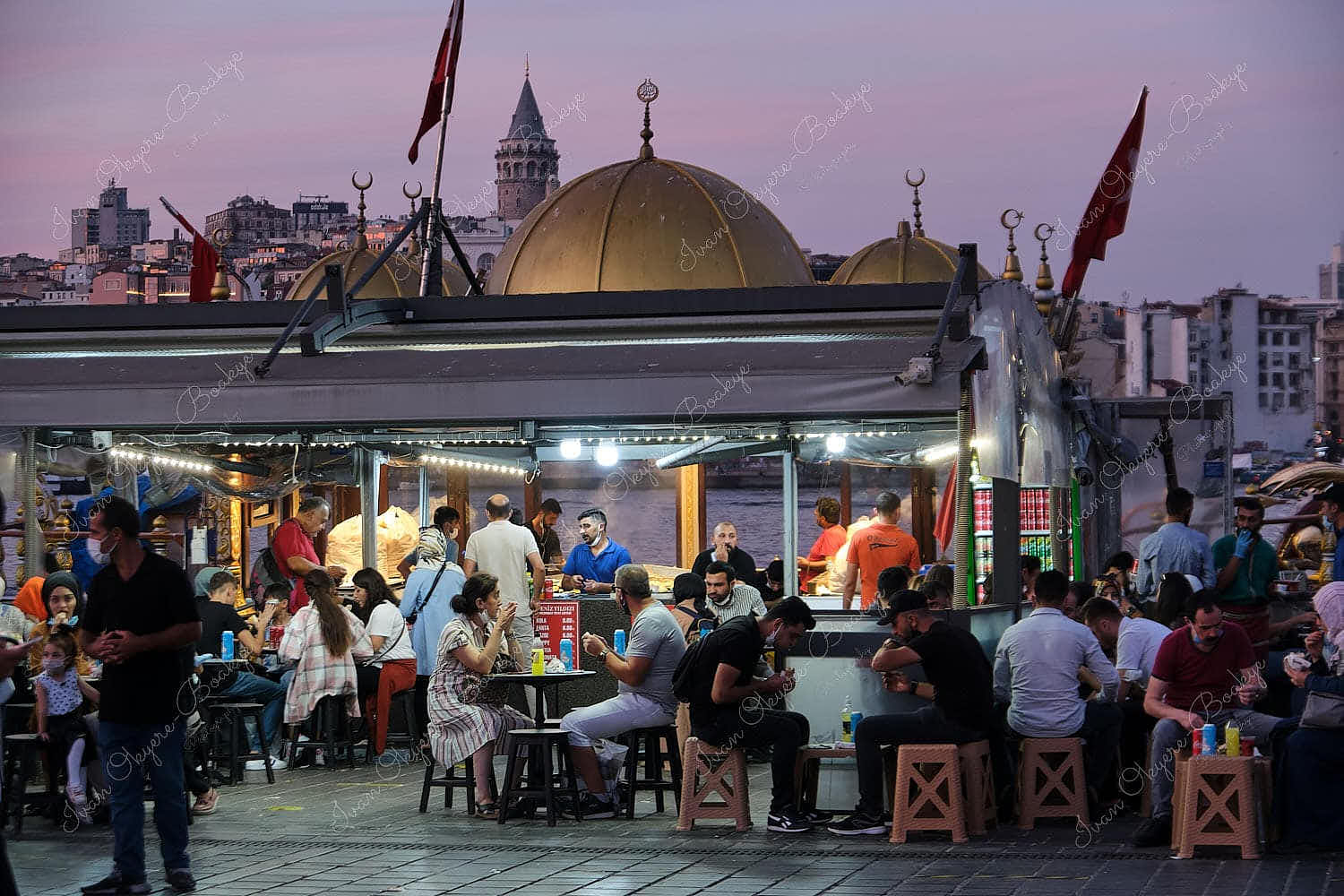 People sitting and eating at a Balik Ekmek moored boat restaurant in Eminonu Square in the evening, Istanbul, Turkey