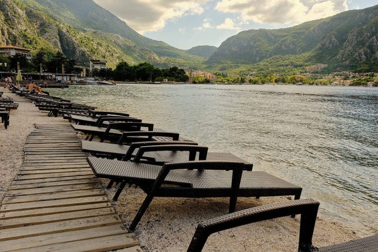 Deck chairs on Kotor Bay promenade beach with mountains in background, Kotor, Montenegro