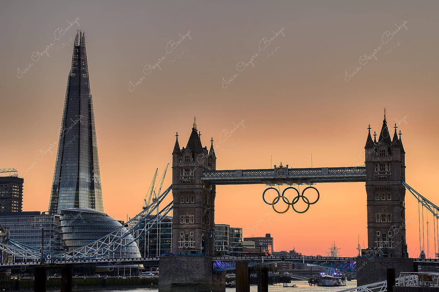 Sunset view of Olympic rings suspended from Tower Bridge during the London 2012 Olympics with City Hall and The Shard in the background, London, UK