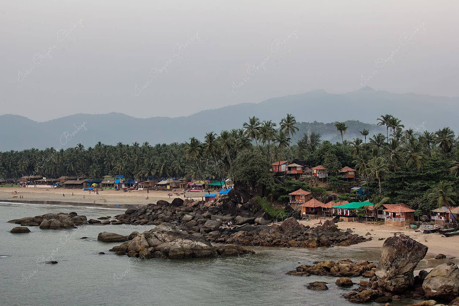Beach huts with coconut trees and mountains in the background at Palolem Beach in Goa, India