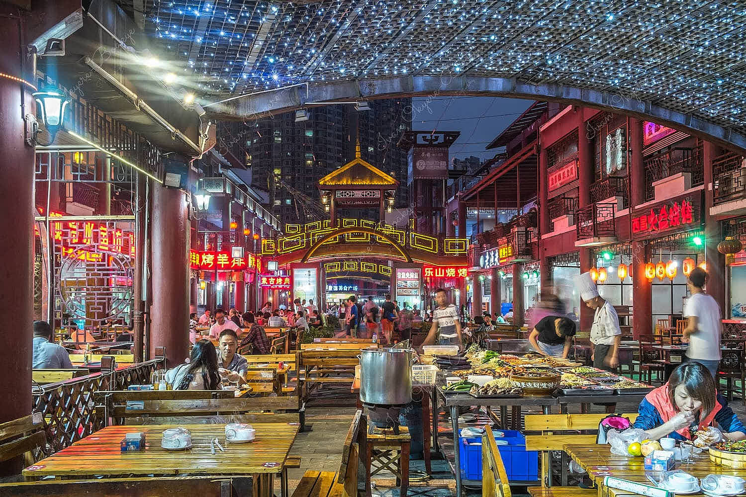 People eating outside in a neon-lit courtyard surrounded by restaurants in Chengdu, China
