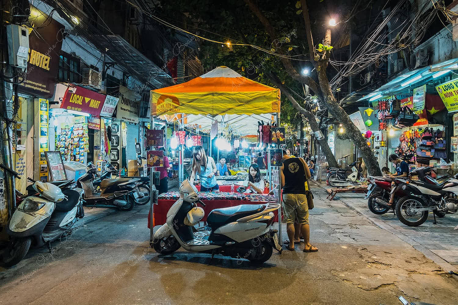 Street vendors and retail shops selling different merchandise in a night market in Hanoi Old Quarter, Vietnam