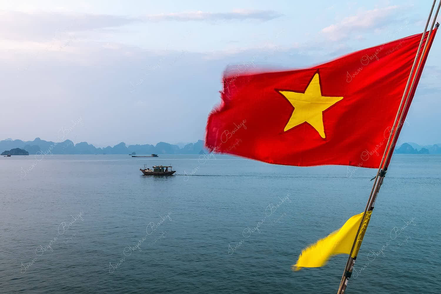 Vietnam Flag fluttering in the wind with fishing boats fishing at sunset in Halong Bay, Vietnam