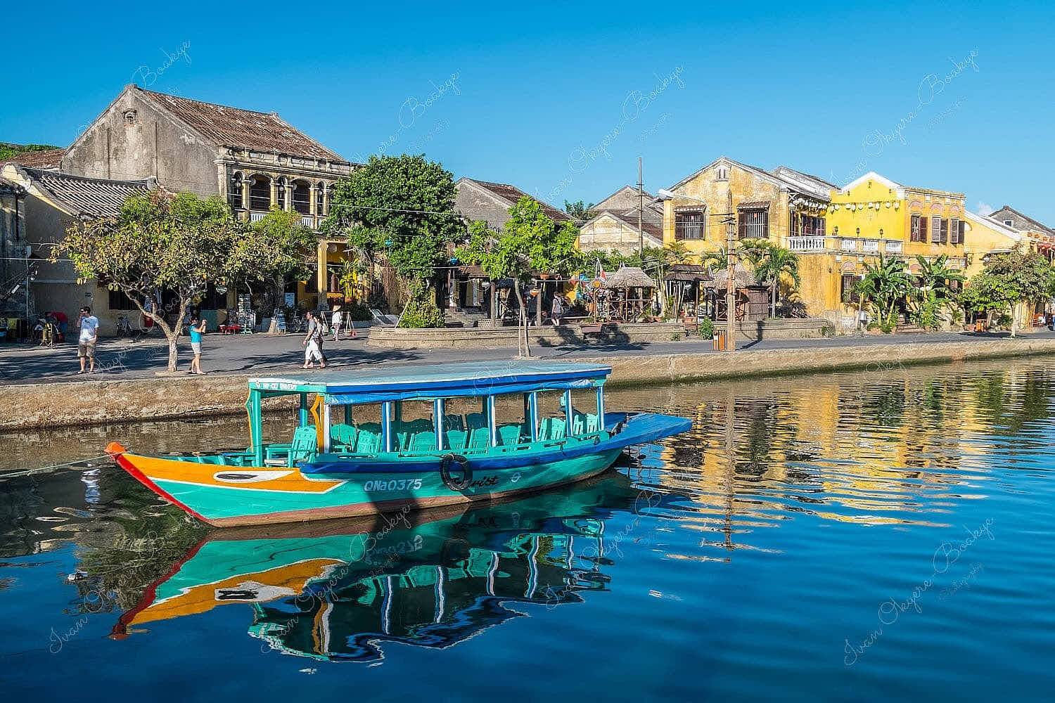 A gorgeous afternoon view of a multicoloured fishing boat and yellow pastel coloured buildings reflecting in the Thu Bon River at Hoi An Old Town riverfront, Vietnam