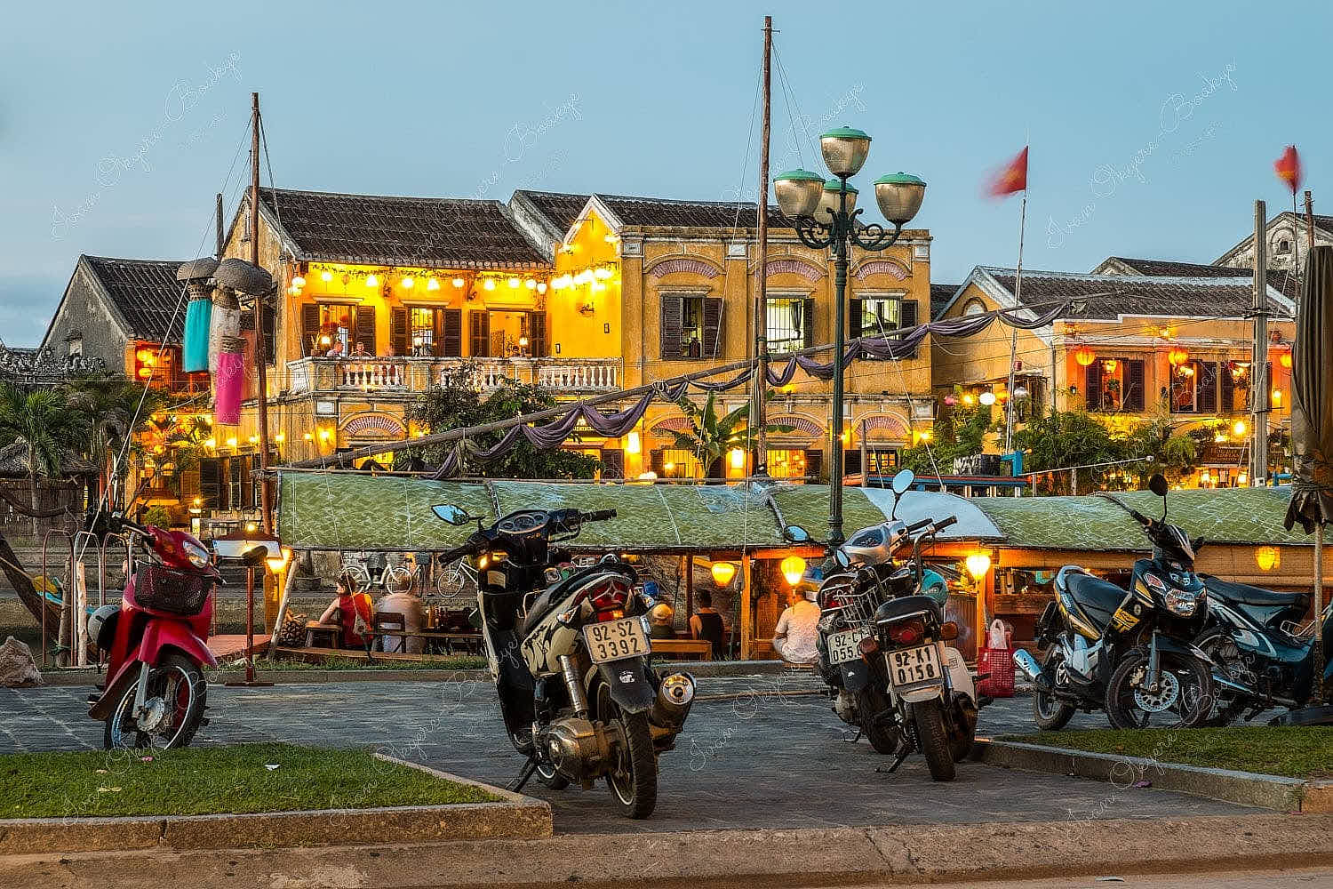 Moored fishing boat restaurant at Thu Bon River with illuminated yellow pastel coloured restaurant buildings at Hoi An Old Town riverfront, Vietnam