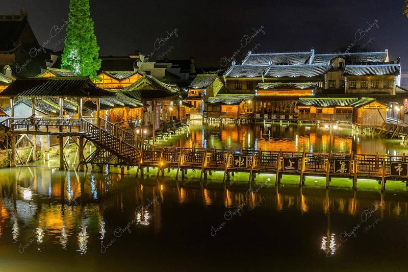 Night time view of flat wooden bridge crossing the canal surrounded by traditional Chinese houses in the historic scenic Wuzhen water town, China Night time view of flat wooden bridge crossing the canal surrounded by traditional Chinese houses in the historic scenic Wuzhen water town, China