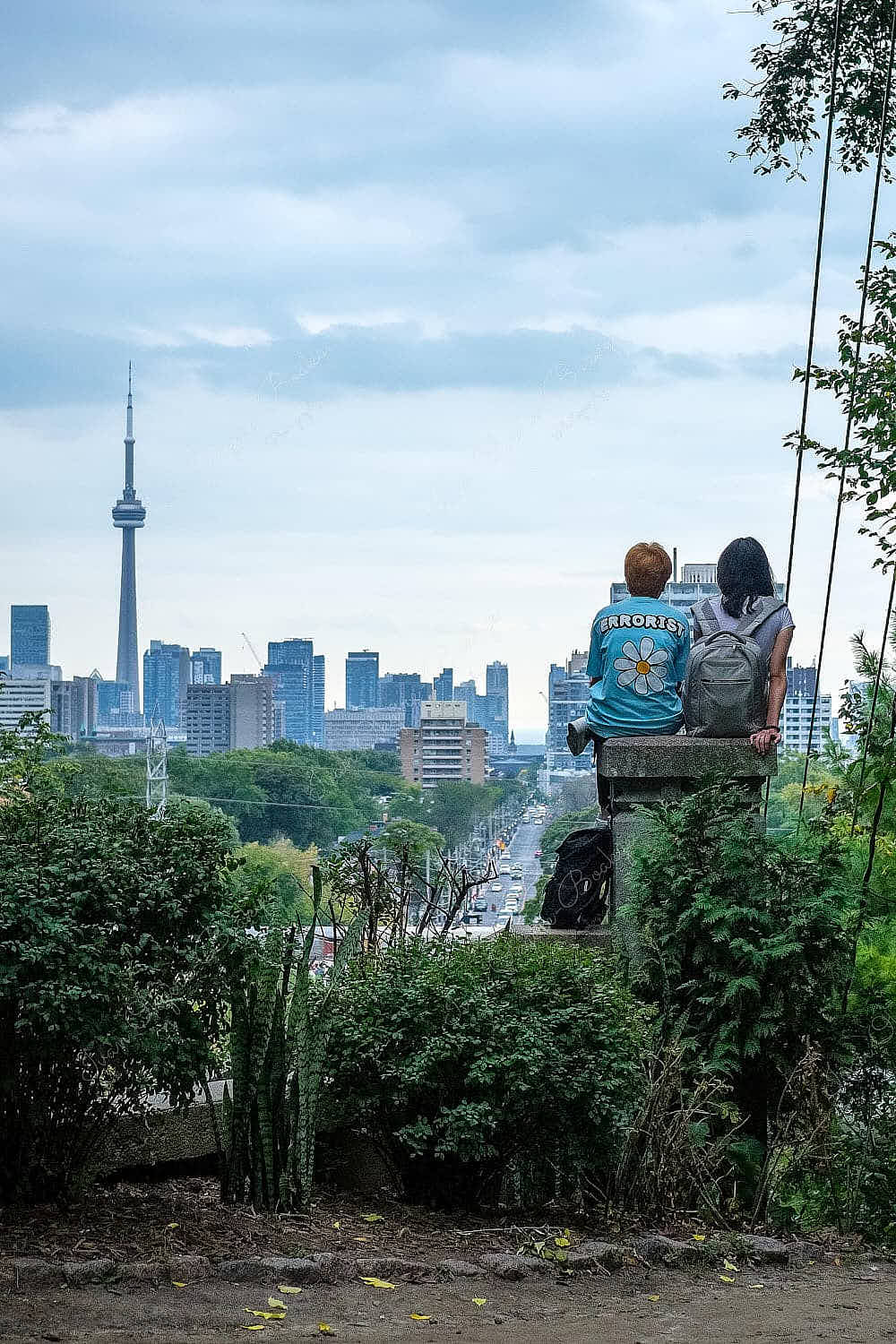 Girlfriends sitting on a wall at the top of a flight of stairs looking down at the Toronto cityscape dominated by the CN Tower, Toronto, Canada