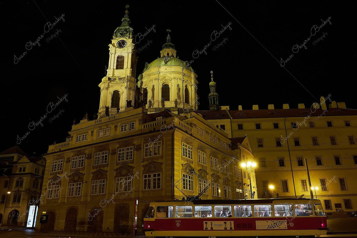 A tram with passengers in front of an illuminated St. Nicholas Church at night, Prague, Czech Republic