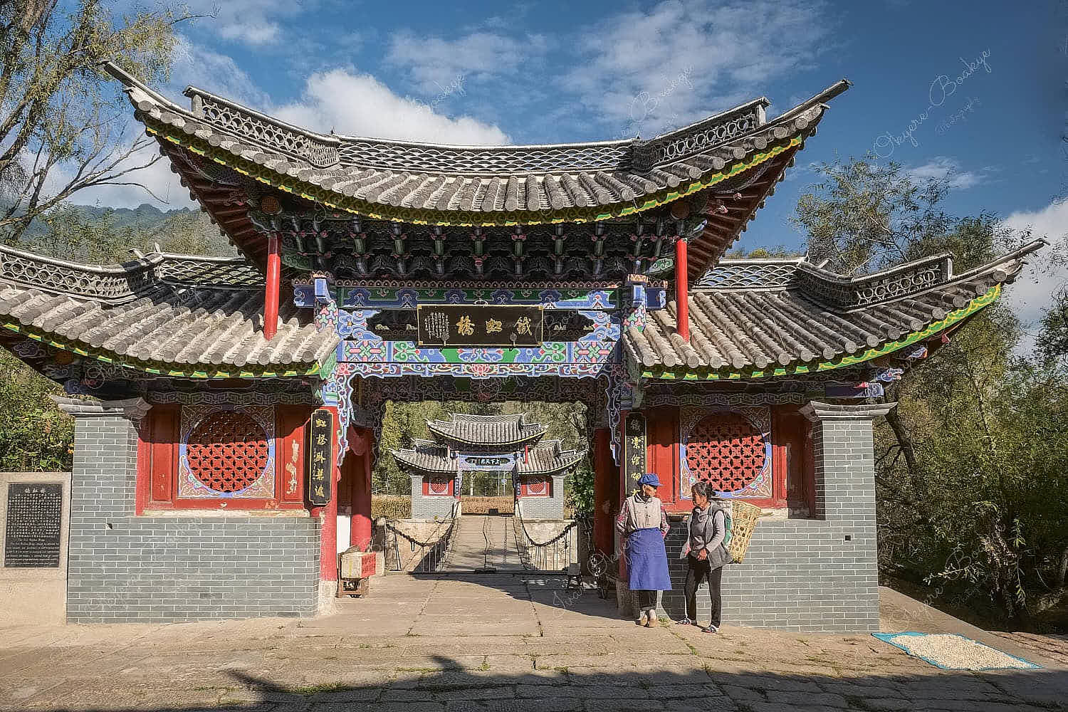 2 women standing in front of the Iron Rainbow Bridge in Stone Drum Town, Shigu Town, Shangri-La, China