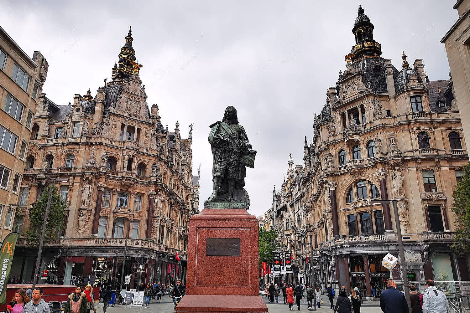 People walking in the streets of Teniersplaats with a David Teniers statue surrounded by elaborate baroque style buildings housing various retail shops on the ground floor, Antwerp, Belgium